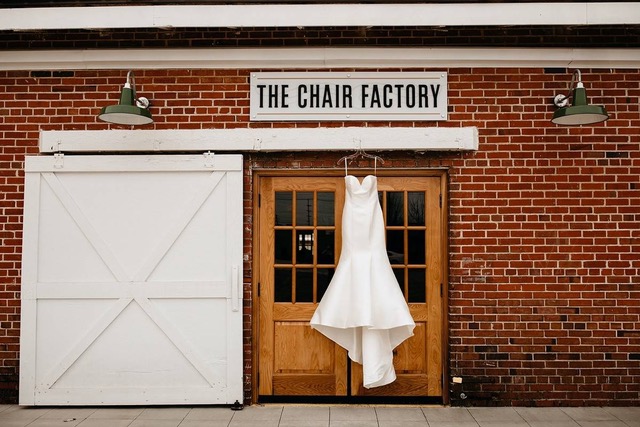 white wedding dress hanging below a The Chair Factory sign