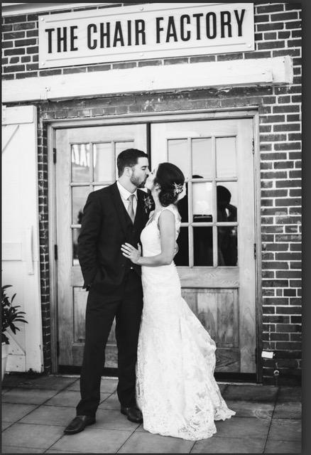 bride and groom kissing underneath a The Chair Factory sign